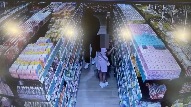 女童推住手推车于货架前拣零食。