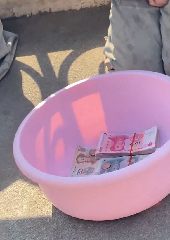 男乞讨面前的盘子放有大量现金。 影片截图