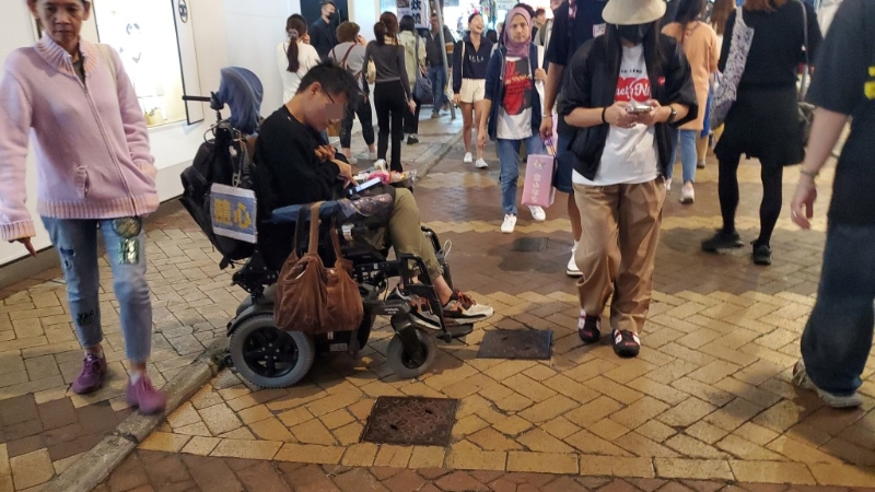铜锣湾渣甸坊有残障人士坐在轮椅上乞讨，并赠送糖果予施舍者。